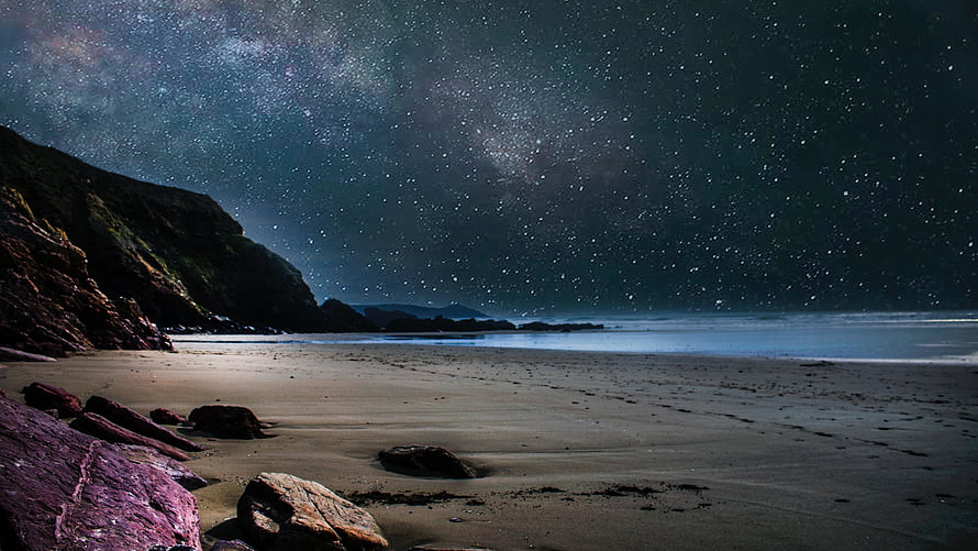 Starry Night Sky Over a Rocky Coastal Beach with Milky Way and Distant Cliffs HD wallpaper