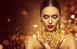 Elegant model holding sparkling gold jewelry against a warm bokeh background HD wallpaper