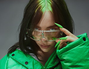 Billie Eilish in a vibrant green jacket and clear protective eyewear HD wallpaper