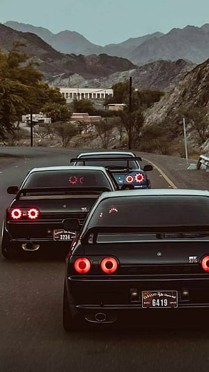 Nissan Skyline GT-R R34 convoy driving on a mountain road with glowing taillights HD phone wallpaper