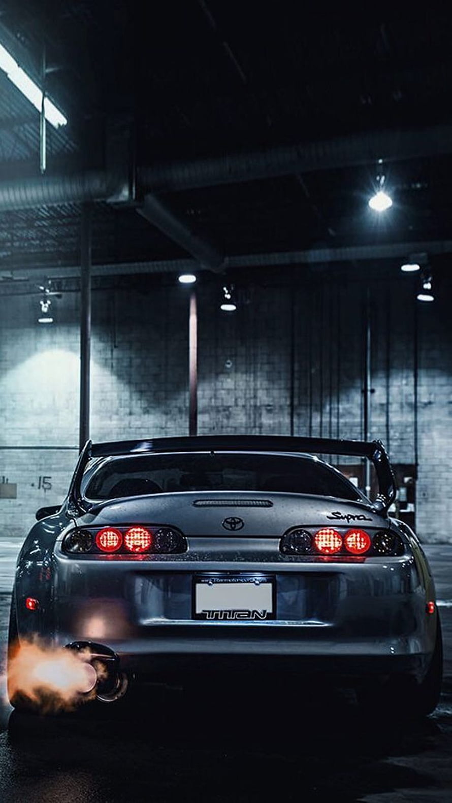 Rear View of a Modified Toyota Supra MK4 with Exhaust Flame in a Dark Garage HD phone wallpaper
