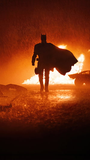 Batman Silhouette Walking Through Fire and Rain in Cinematic Dark Atmosphere HD phone wallpaper