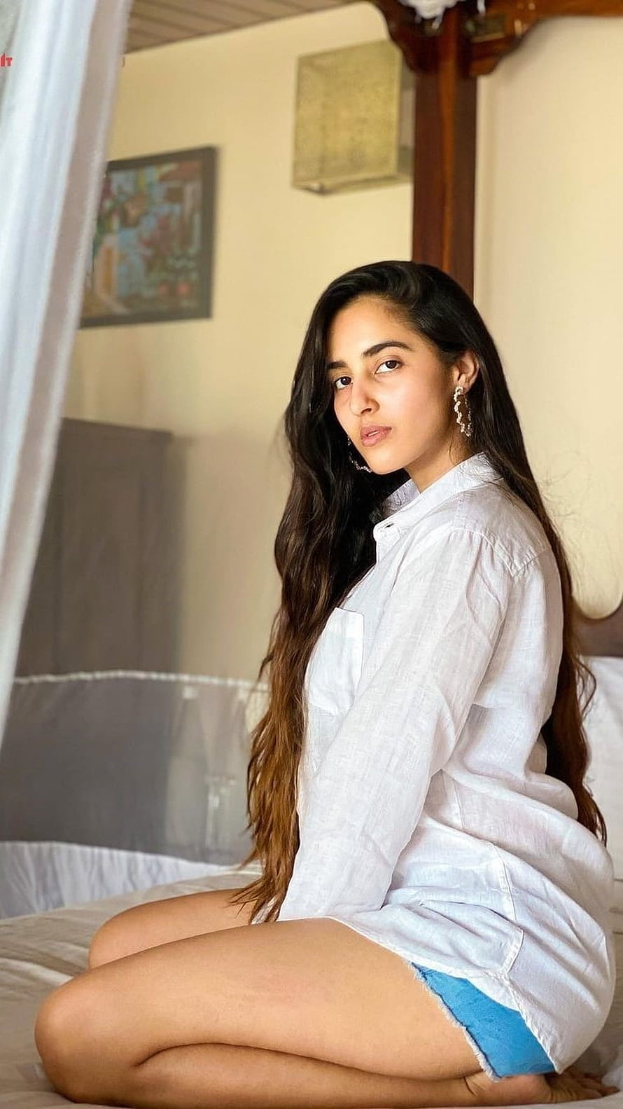 Simrat Kaur Sitting on Bed in White Linen Shirt and Blue Denim Shorts HD phone wallpaper