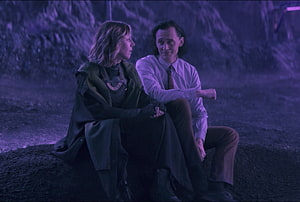 Loki and Sylvie seated together in a dim purple-lit scene from the Marvel series HD wallpaper