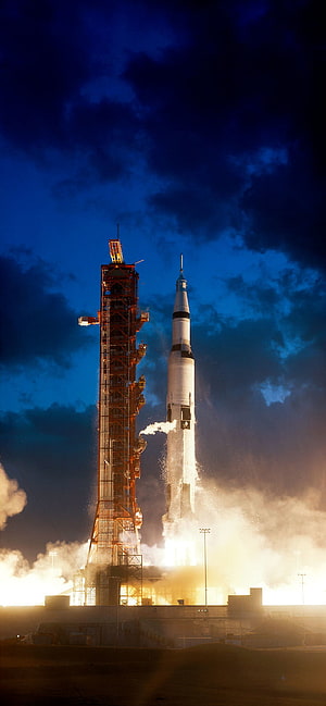 Saturn V rocket lifting off from launch pad at night with fiery exhaust and smoke HD phone wallpaper