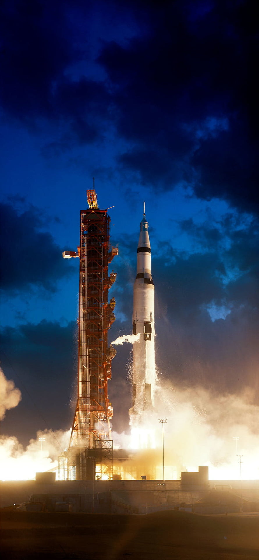 Saturn V rocket lifting off from launch pad at night with fiery exhaust and smoke HD phone wallpaper