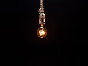 Glowing Edison bulb suspended by a rope against a dark background HD wallpaper