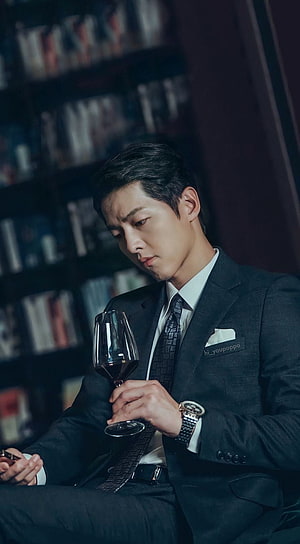 Vincenzo K-drama still of a man in a dark suit holding a glass of red wine in a library HD phone wallpaper