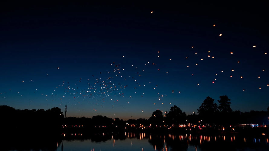 Glowing Sky Lanterns Floating Over a Calm Lake at Night HD wallpaper