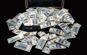 Stacks of US hundred dollar bills spilling from an open black briefcase against a dark background HD wallpaper