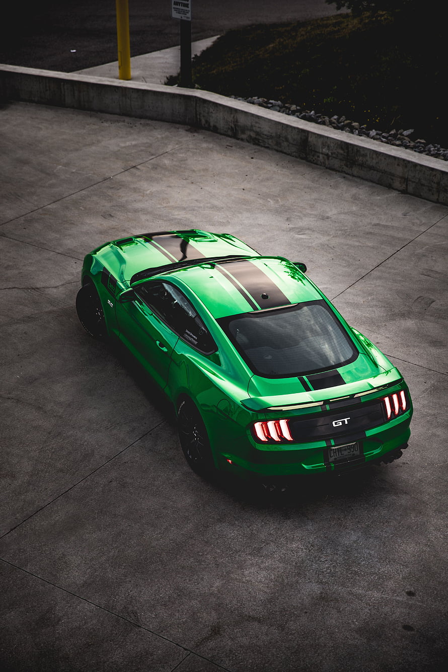 Ford Mustang GT in vibrant green with black racing stripes captured from a high-angle rear view on concrete HD phone wallpaper