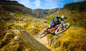 Downhill Mountain Biker Launching Off a Dirt Jump in a Rugged Mountain Valley HD wallpaper