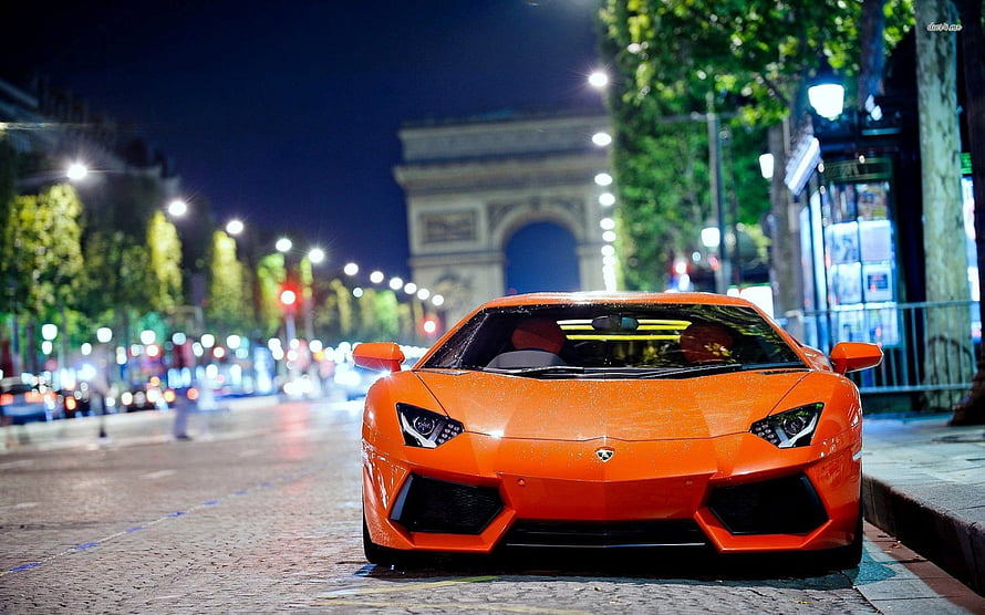 Orange Lamborghini Aventador parked on a Parisian street at night with the Arc de Triomphe in the background HD wallpaper