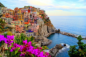 Colorful cliffside village in Italy overlooking the Mediterranean Sea with vibrant bougainvillea in the foreground HD wallpaper