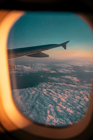 Aerial View of Clouds and Airplane Wing Through a Window at Sunset HD phone wallpaper