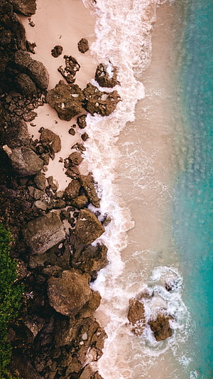 Aerial View of Rocky Shoreline with Turquoise Sea Waves and White Foam HD phone wallpaper