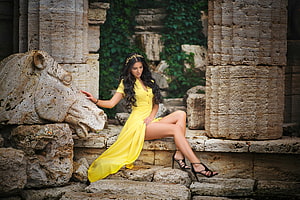 Elegant Woman in Yellow Dress Seated on Ancient Stone Ruins with Carved Horse Head HD wallpaper