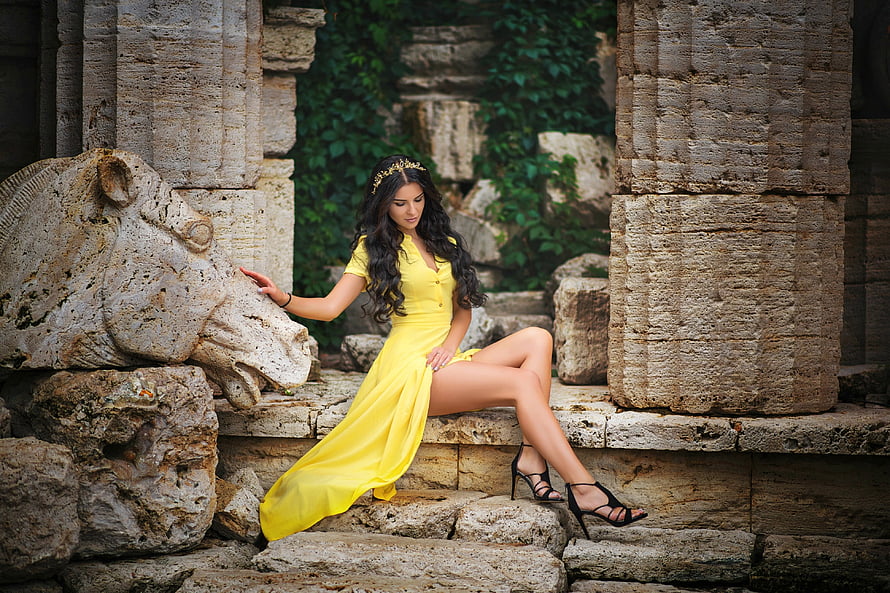 Elegant Woman in Yellow Dress Seated on Ancient Stone Ruins with Carved Horse Head HD wallpaper