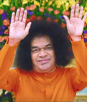 Sathya Sai Baba in Orange Robe with Hands Raised Against a Vibrant Floral Background HD phone wallpaper