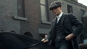 Tommy Shelby in a three-piece suit and flat cap beside a horse in an industrial brick alley HD wallpaper