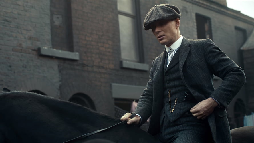 Tommy Shelby in a three-piece suit and flat cap beside a horse in an industrial brick alley HD wallpaper