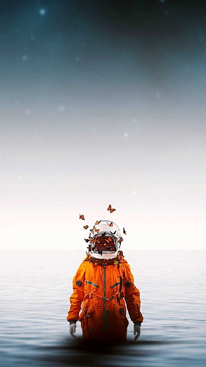 Astronaut in Orange Suit Standing in Calm Ocean with Swirling Butterflies HD phone wallpaper