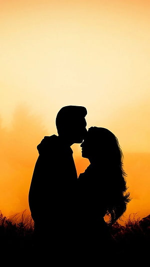 Romantic couple silhouette sharing a kiss against a warm golden sunset sky HD phone wallpaper
