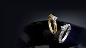 Elegant Diamond Engagement Rings in Gold and Silver on Dark Reflective Surface HD wallpaper