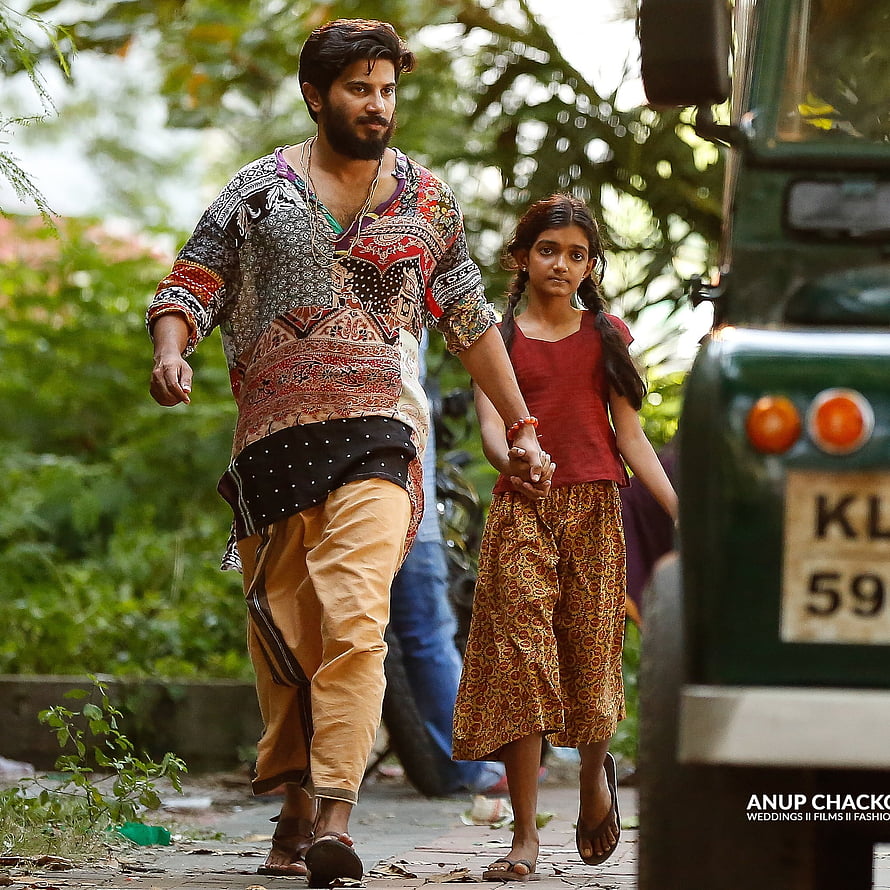 Dulquer Salman and young girl walking through lush greenery in traditional Indian attire HD phone wallpaper