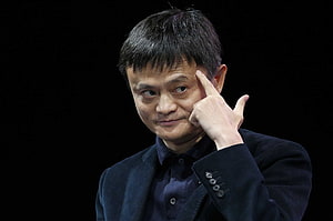 Jack Ma in a dark suit with finger to temple against a black background HD wallpaper