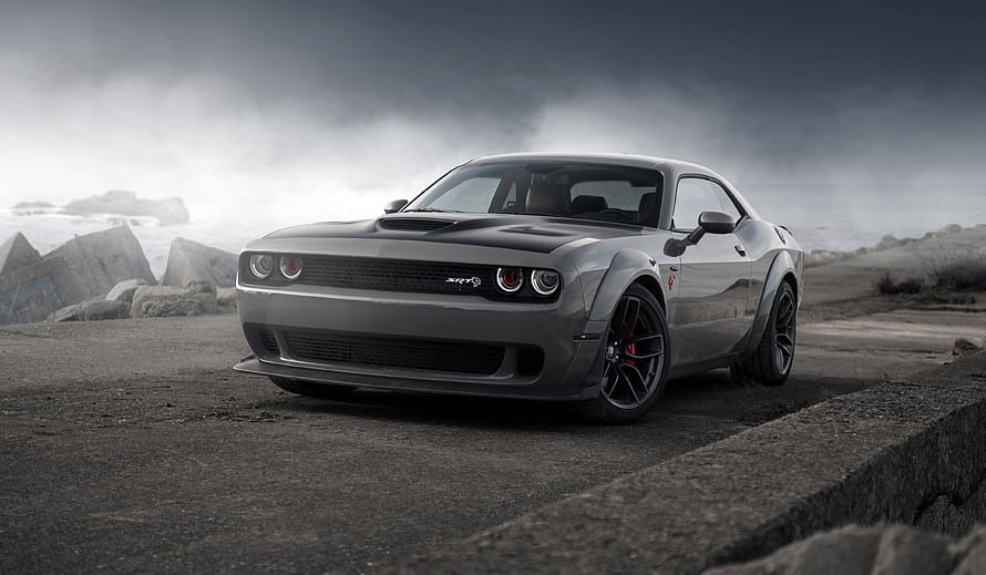 Dodge Challenger SRT muscle car parked on a rugged coastal cliff under a dramatic overcast sky HD wallpaper