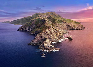 Aerial View of Rugged Coastal Island at Sunset with Dramatic Rocky Cliffs and Calm Ocean Waters HD wallpaper