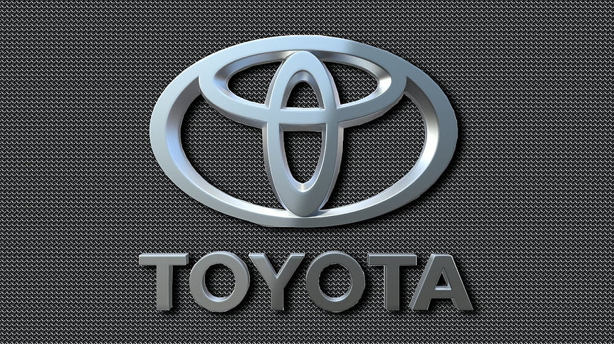 Sleek Chrome Toyota Emblem on Dark Carbon Fiber Textured Surface HD wallpaper