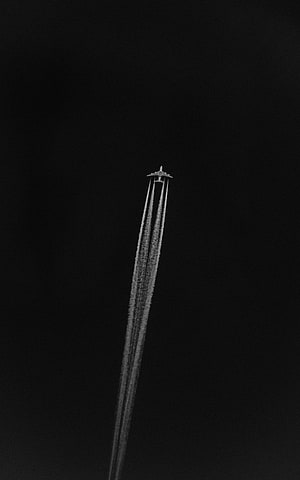 Minimalist Black and White Airplane Leaving Contrails Against a Dark Sky HD phone wallpaper