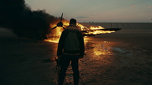 Dunkirk Movie Scene: Soldier Silhouette Before Burning Aircraft on Beach at Dusk HD wallpaper