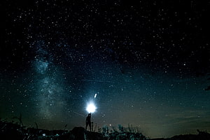 Silhouette of a person holding a bright light beneath the Milky Way and starry night sky HD wallpaper