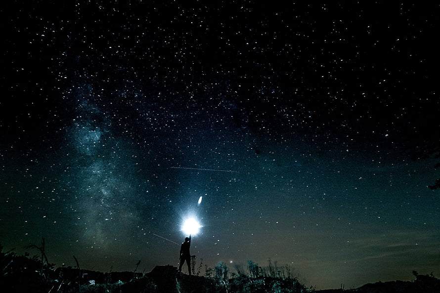Silhouette of a person holding a bright light beneath the Milky Way and starry night sky HD wallpaper