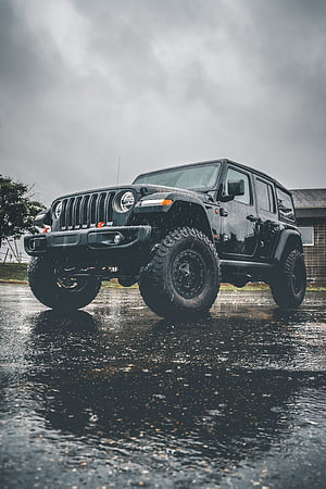Black Jeep Wrangler Unlimited with Off-Road Tires on Wet Asphalt Under Stormy Sky HD phone wallpaper