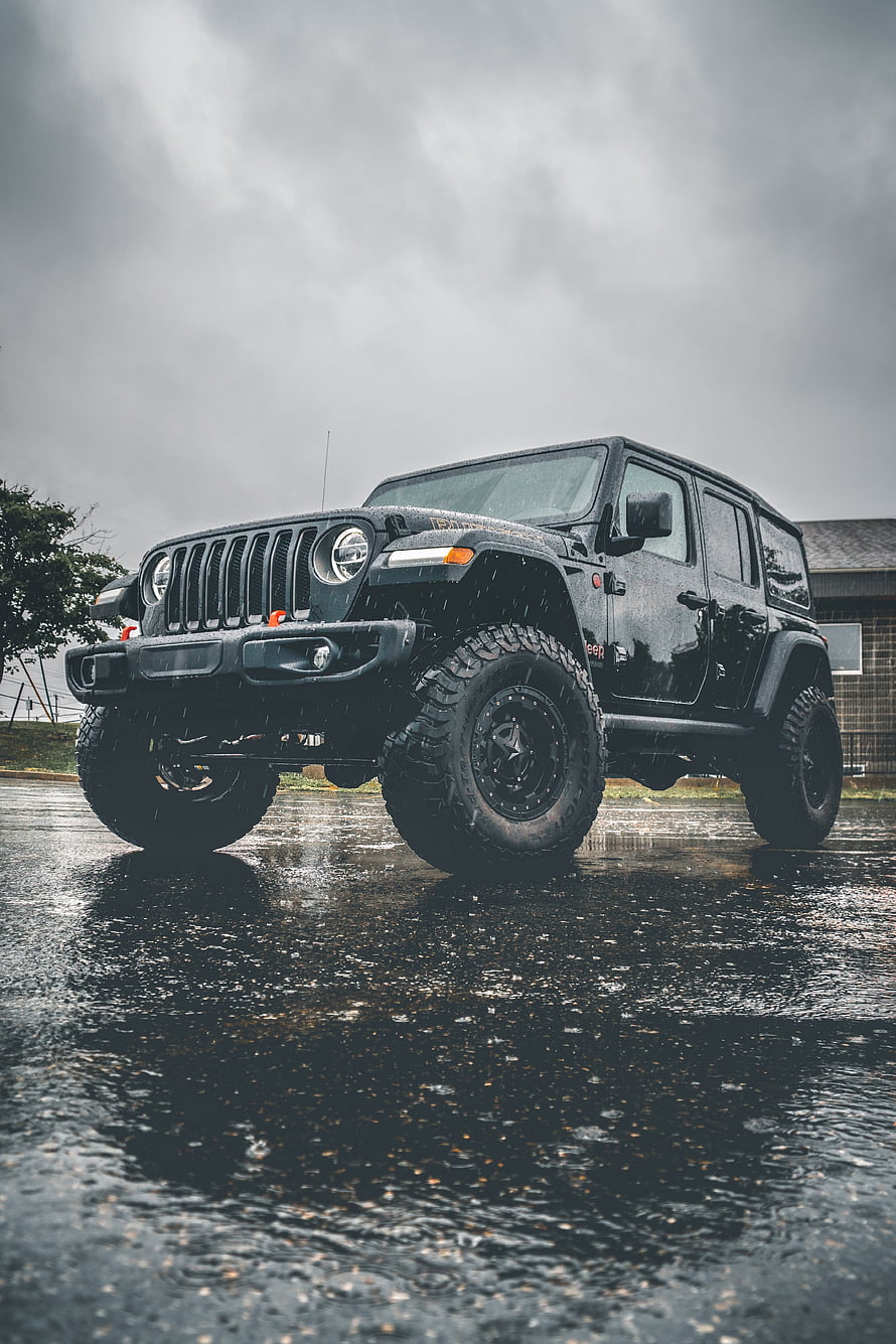 Black Jeep Wrangler Unlimited with Off-Road Tires on Wet Asphalt Under Stormy Sky HD phone wallpaper