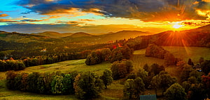 Golden sunset over rolling hills with sun rays illuminating autumn trees and green fields HD wallpaper
