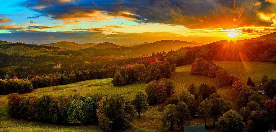 Golden sunset over rolling hills with sun rays illuminating autumn trees and green fields HD wallpaper