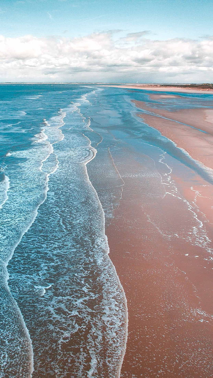 Aerial View of Turquoise Ocean Waves Rolling onto a Wide Sandy Beach Under a Cloudy Sky HD phone wallpaper
