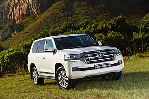 White Toyota Land Cruiser 200 SUV Parked on Grassy Hillside with Rocky Mountain Backdrop HD wallpaper
