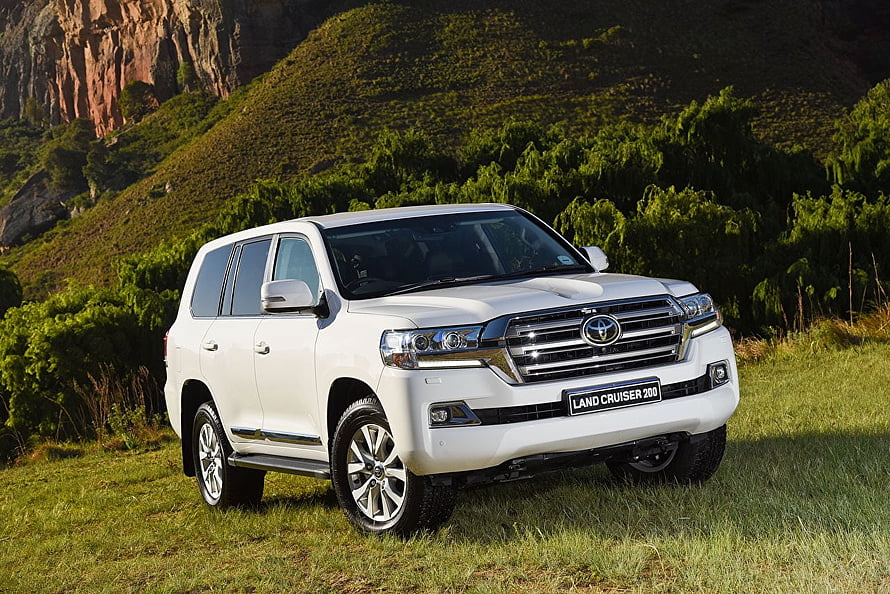 White Toyota Land Cruiser 200 SUV Parked on Grassy Hillside with Rocky Mountain Backdrop HD wallpaper