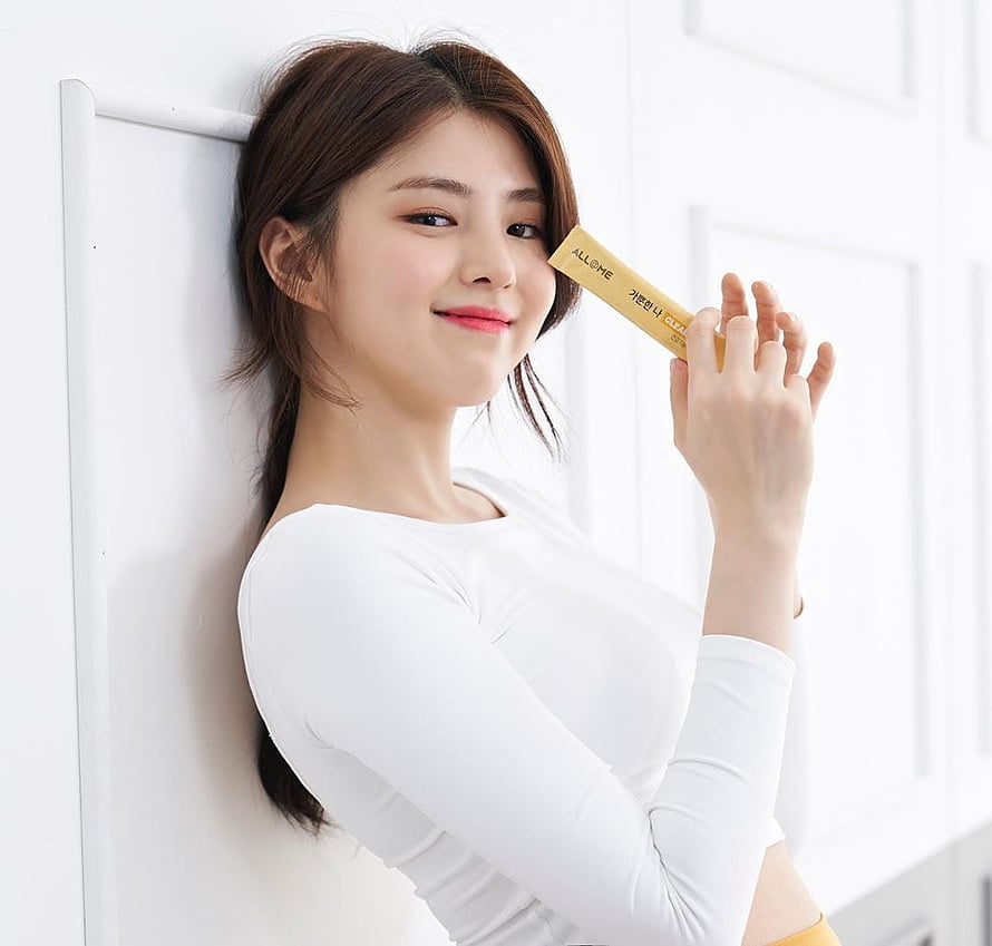 Han So Hee in a white top holding a gold cosmetic tube against a white paneled wall HD wallpaper