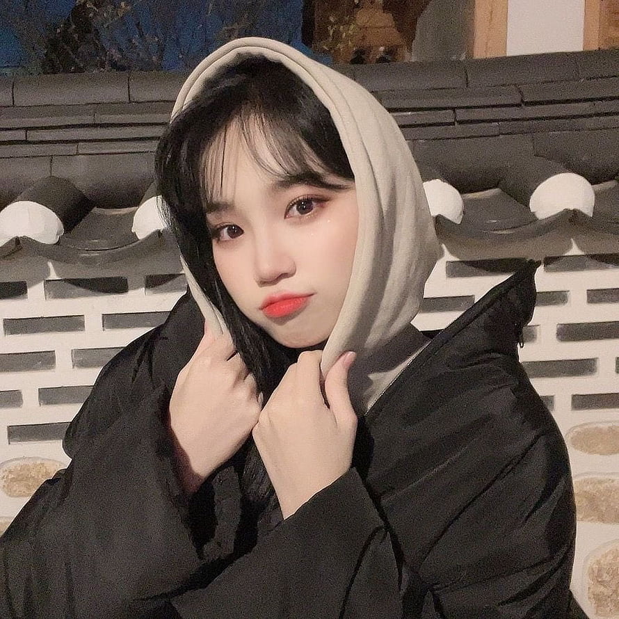 Kim Chaewon in a beige hood and black jacket against a traditional tiled wall HD phone wallpaper