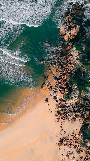 Aerial View of Turquoise Ocean Waves Crashing onto Rocky Coastline and Sandy Beach HD phone wallpaper