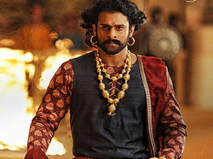 Prabhas as Baahubali in epic period costume with gold jewelry and dramatic fire backdrop HD wallpaper