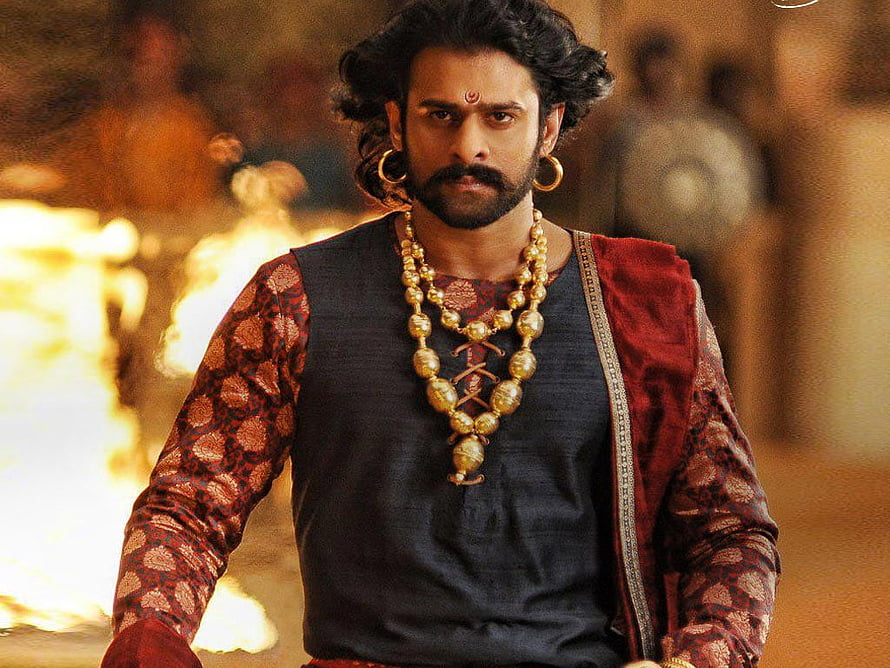 Prabhas as Baahubali in epic period costume with gold jewelry and dramatic fire backdrop HD wallpaper