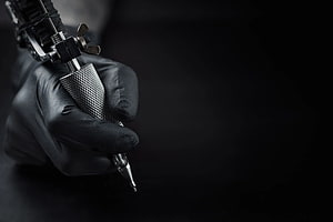 Close-up of a gloved hand holding a professional tattoo machine against a dark background HD wallpaper